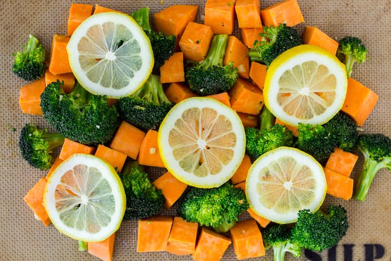 Cubed Sweet potatoes and broccoli on a silpat baking mat with lemon slices on top