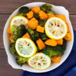 Overhead view of lemon roasted broccoli and sweet potatoes in a white serving dish on a wood backdrop with a blue napkin