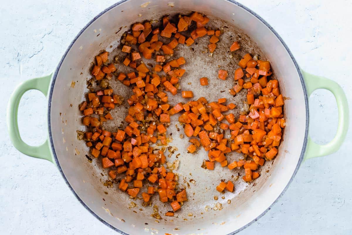 Carrots, shallot and garlic cooking in a dutch oven over a white background
