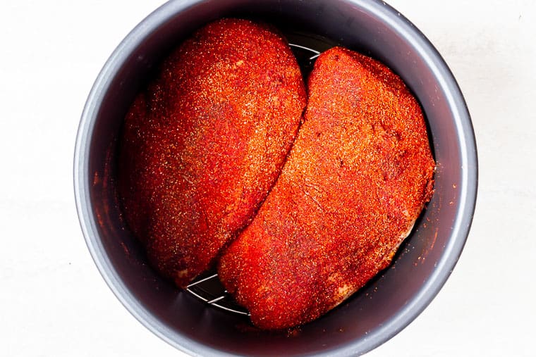 2 large chicken breasts with a chipotle chili dry run on them inside of an instant pot over a white background