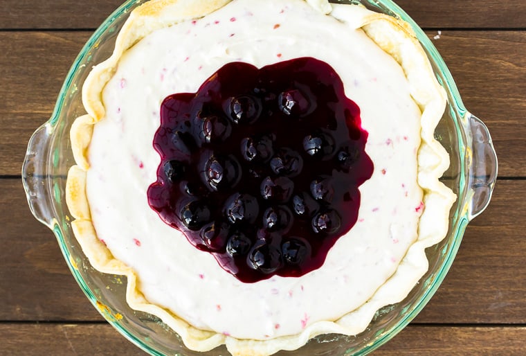 No Bake Raspberry Cheesecake topped with blueberry sauce in a pie dish over a wood backdrop