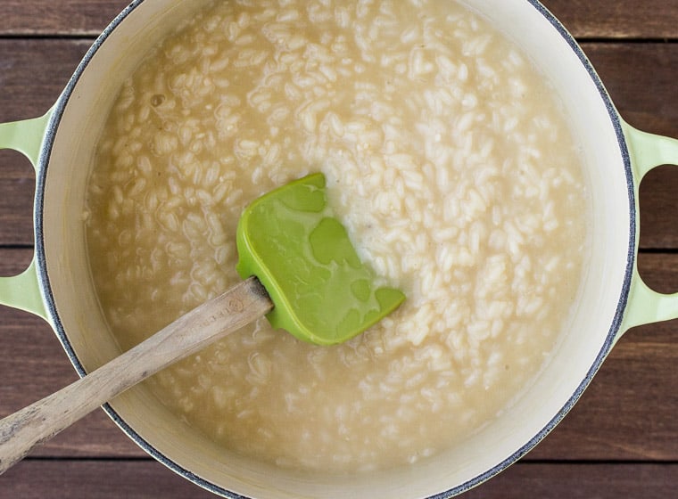 Rice Cooking in Liquid in a Dutch Oven with a green silicone and wood spatula in it over a wood background
