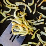 Close up of roasted fennel on a silver spatula on a baking sheet