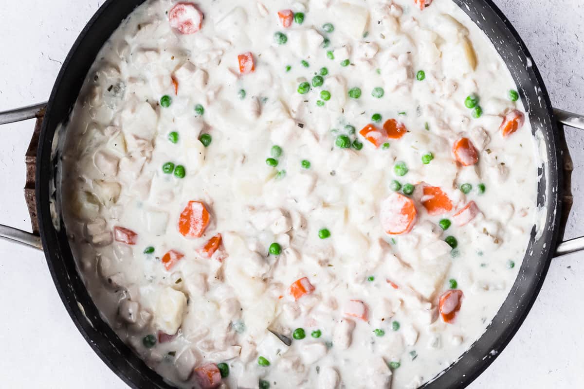 Chicken, peas, carrots, and potatoes in a cream sauce in a black skillet