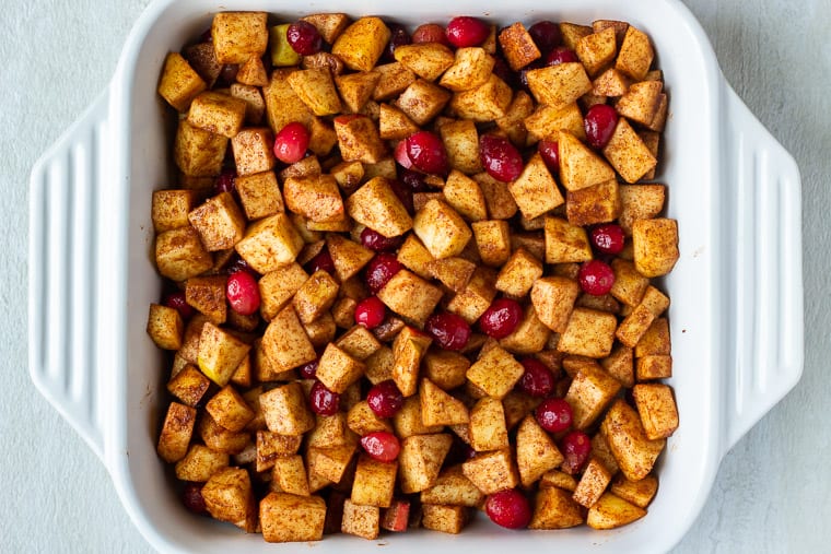 Seasoned apples and cranberries in a square, white casserole dish