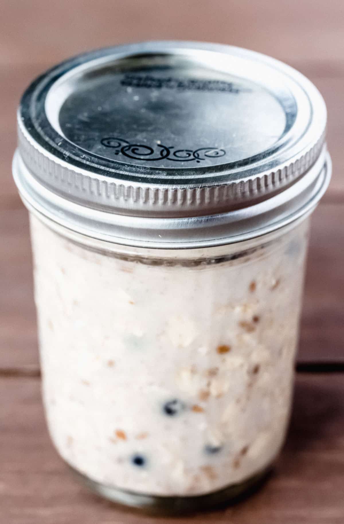 Blueberry oats in a mason jar with the lid on on a wood background