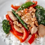 Close up of a serving of chicken peanut stir fry on rice on a white plate with text overlay.