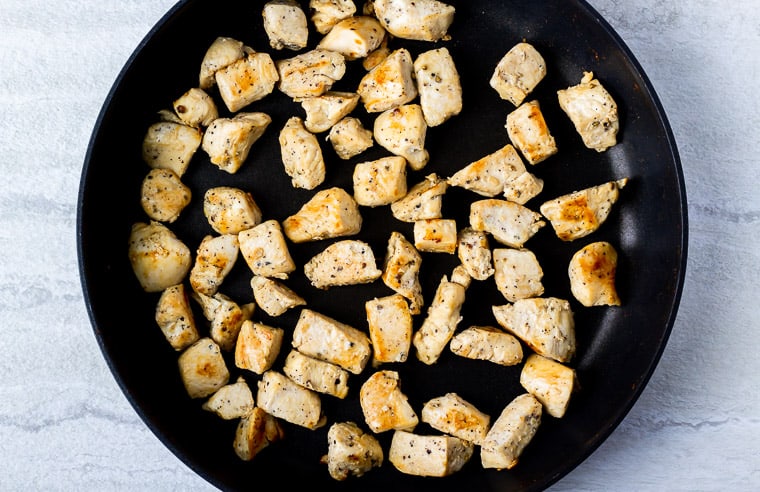 Cubes of chicken cooked in a black skillet over a white background
