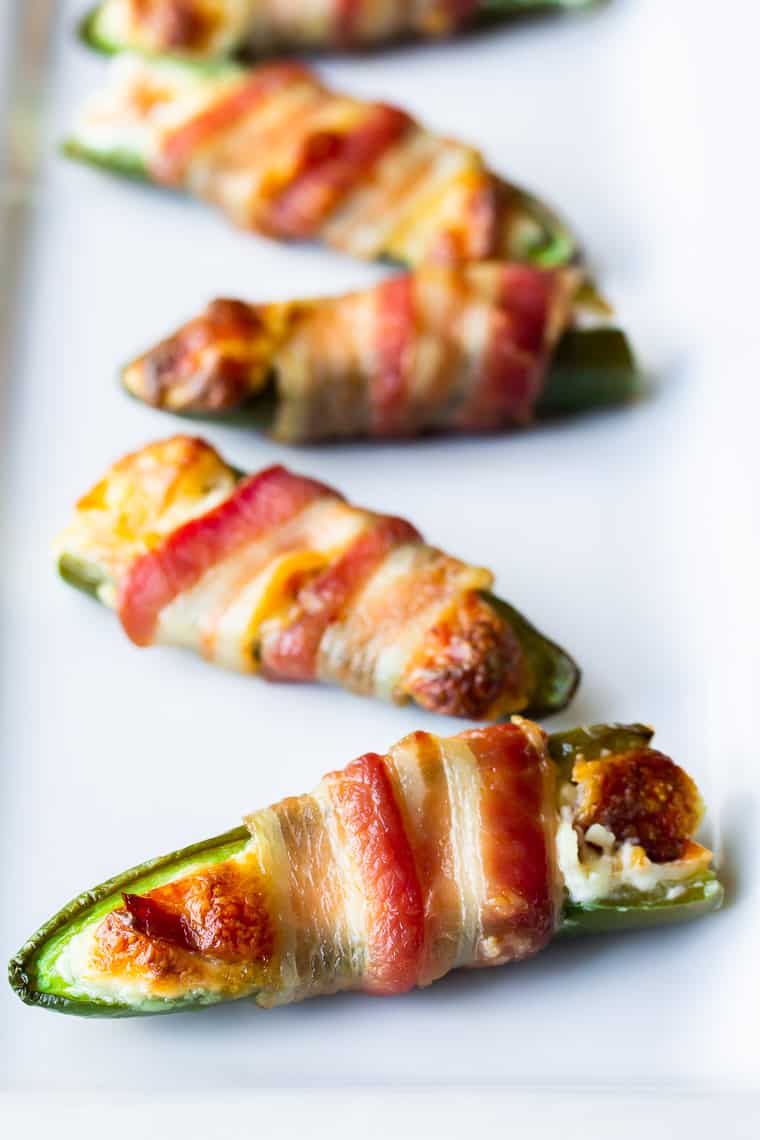 Bacon wrapped jalapeno peppers on a white rectangular serving tray