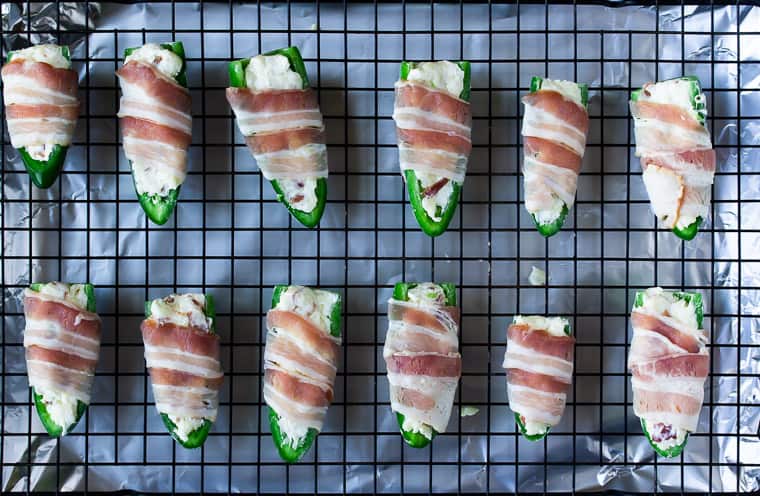 Jalapeno peppers stuffed with cream cheese and bacon, wrapped in bacon on a baking rack
