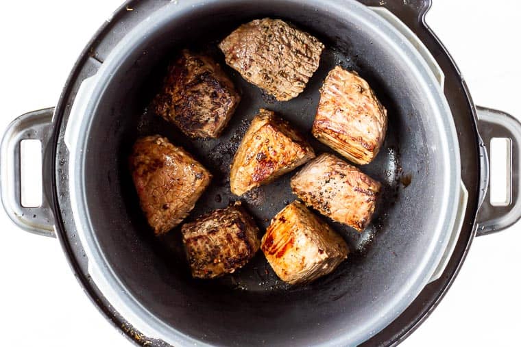 Browned beef cubes in the bottom of a pressure cooker over a white background