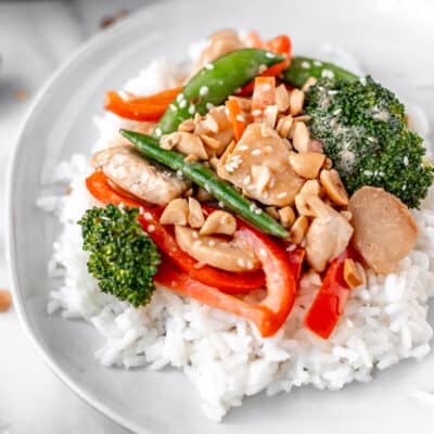 Chicken peanut story fry with vegetables and rice on a white plate.