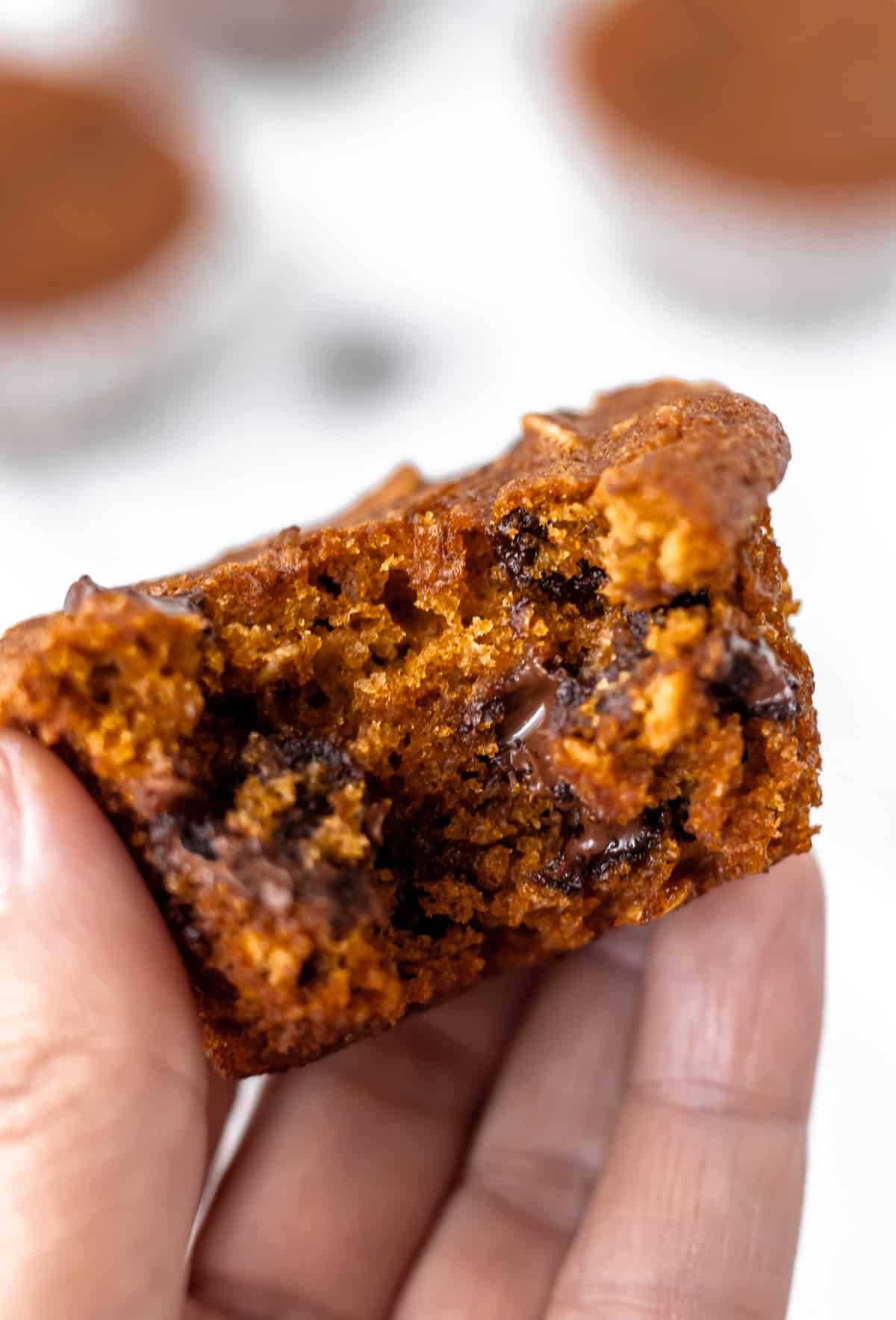 A hand holding up a pumpkin chocolate chip muffin with a bite taken out of it.