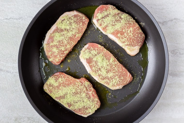 Pork Chops with Ranch Seasoning on top cooking in a black skillet over a white background