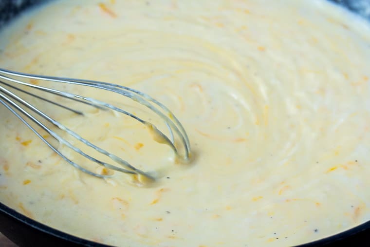 Cheese Sauce with a Whisk in a Cast Iron Skillet