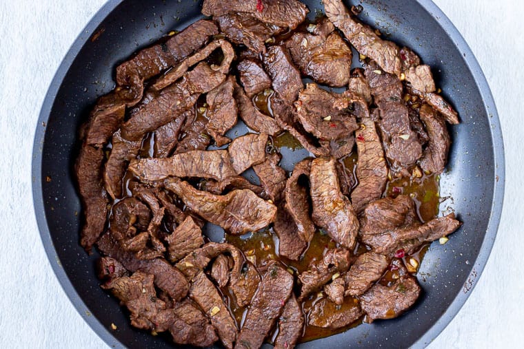 Fajita steak strips cooking in a large black skillet
