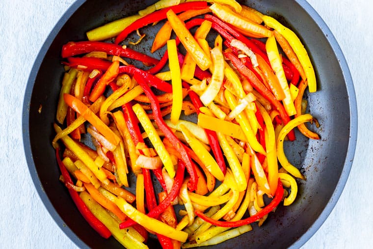 Pepper and onion strips cooking in a large black skillet