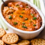 barbecue chicken dip with crackers and celery around it and a spoon in it