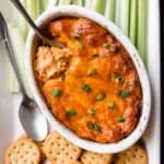 Overhead of barbecue chicken dip with a spoon it and crackers and celery sticks around it