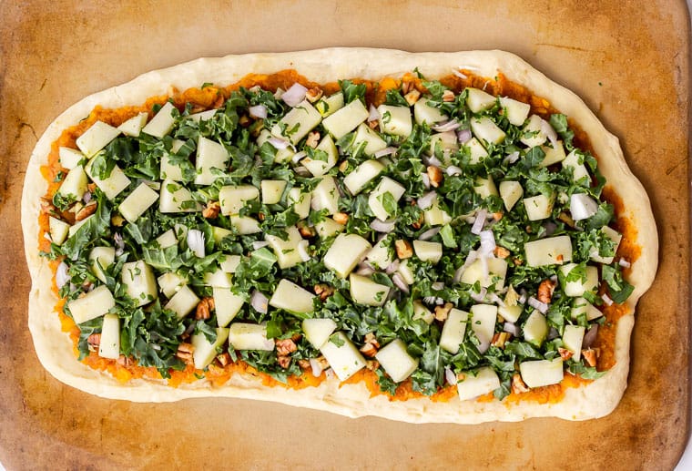 Pizza dough topped with butternut squash puree, kale, apples, shallots, and walnuts