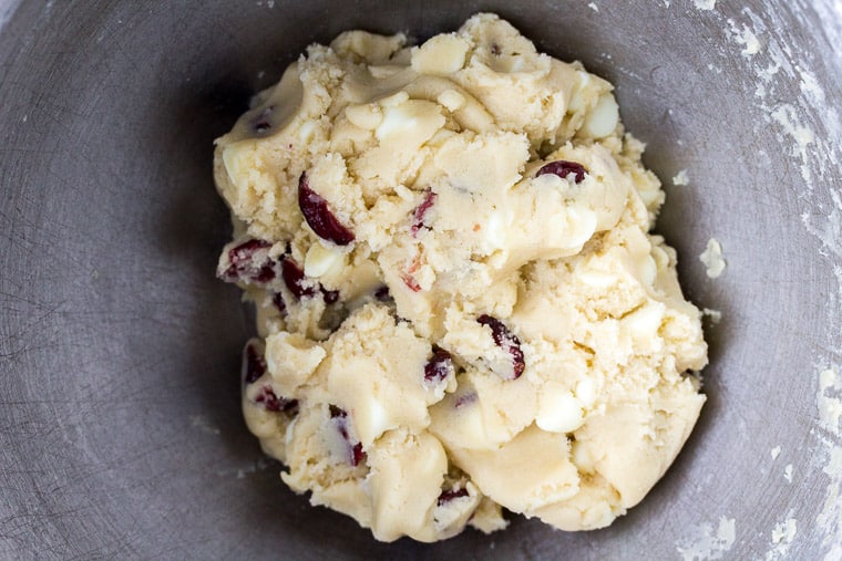 Cookie dough with cranberries and white chocolate chips mixed in in a silver bowl
