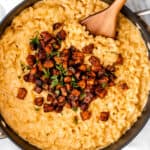 Overhead of a skillet of mac and cheese topped with spiced sweet potatoes with a wood server in it.