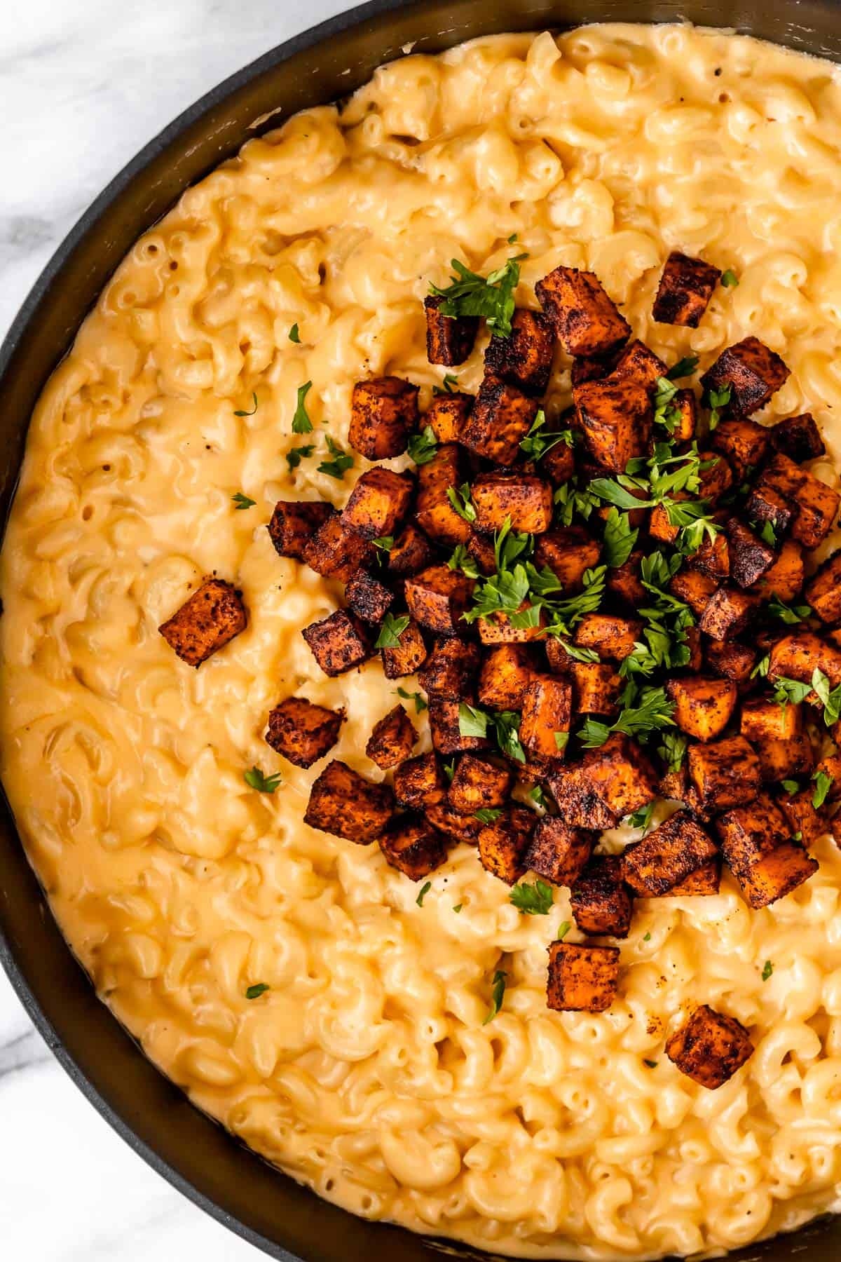 Overhead of half a skillet with mac and cheese topped with roasted sweet potatoes in it.