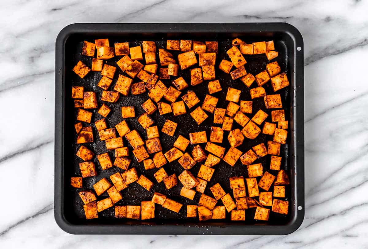 Cubes of sweet potatoes seasoned with chili powder and paprika on a baking sheet.