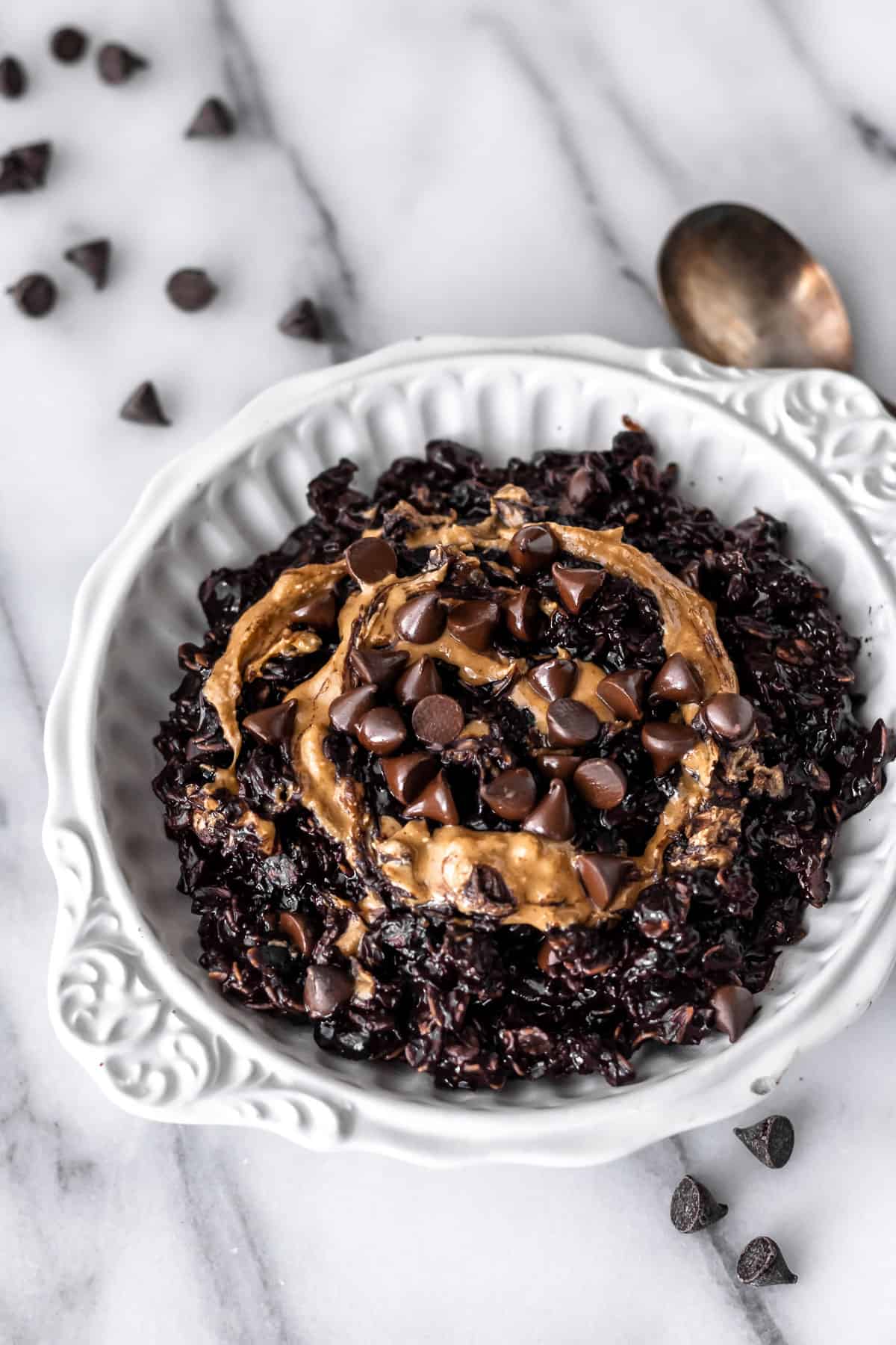 A white bowl of dark chocolate peanut butter oatmeal with chocolate chips and a spoon around it.