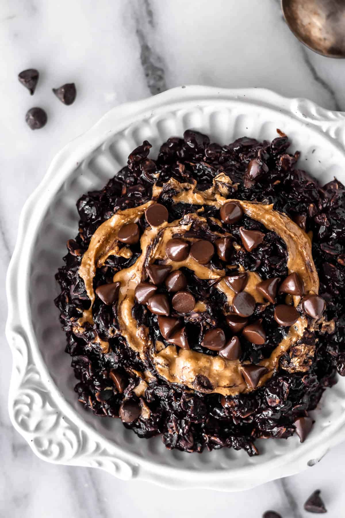Overhead of a white bowl filled with dark chocolate peanut butter oatmeal and topped with peanut butter and chocolate chips.
