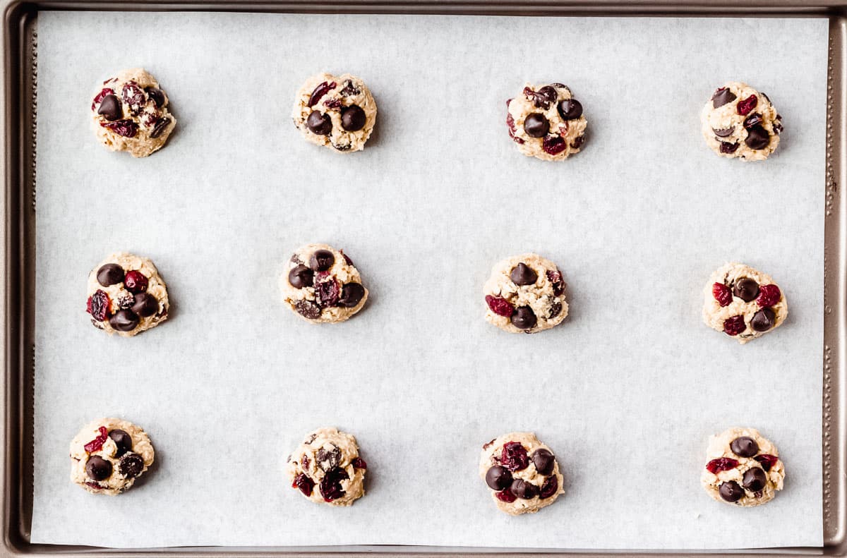 Cranberry oatmeal chocolate chip dough balls on a parchment paper lined baking sheet