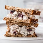 Cranberry Walnut chicken salad sandwich cut in half and stacked on top of each other on a white plate with a gray background