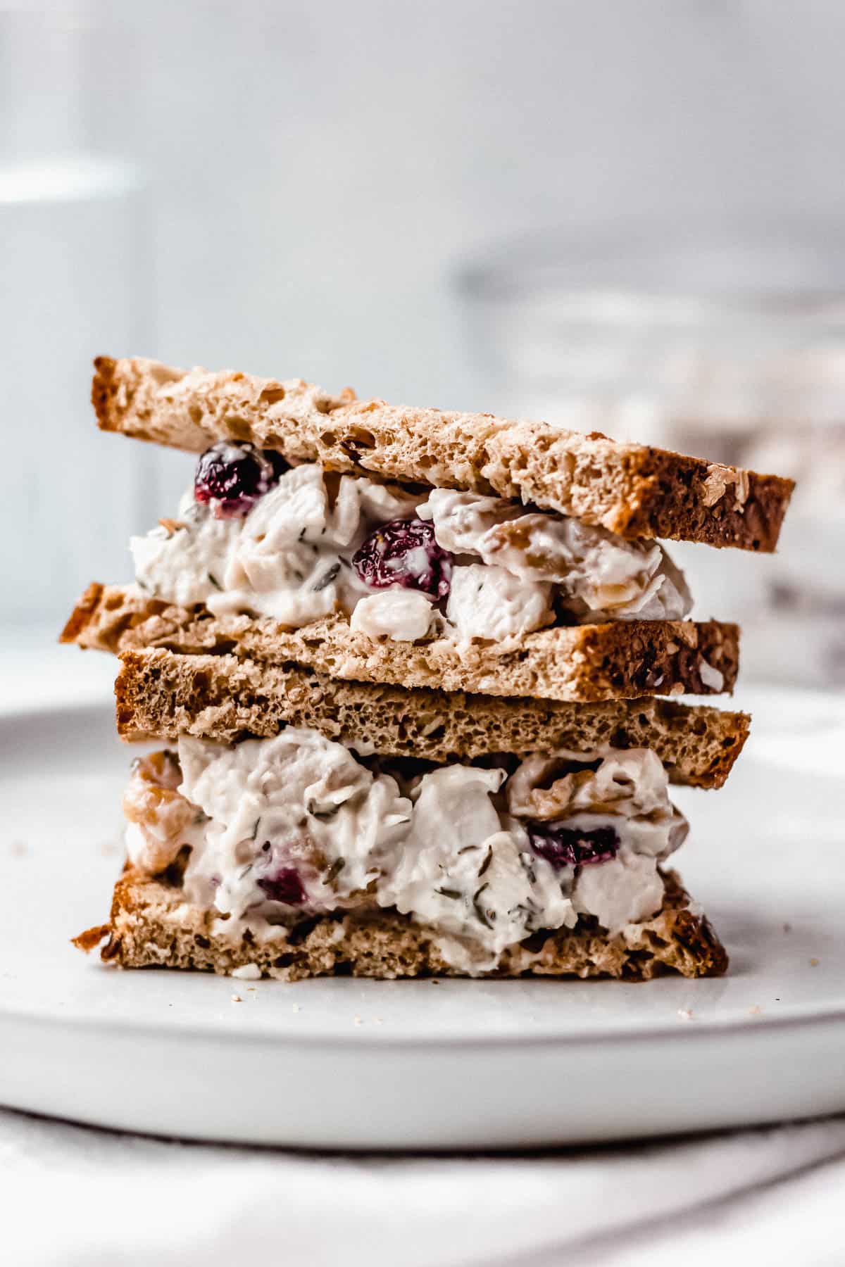 Cranberry Walnut chicken salad sandwich cut in half and stacked on top of each other on a white plate with a gray background