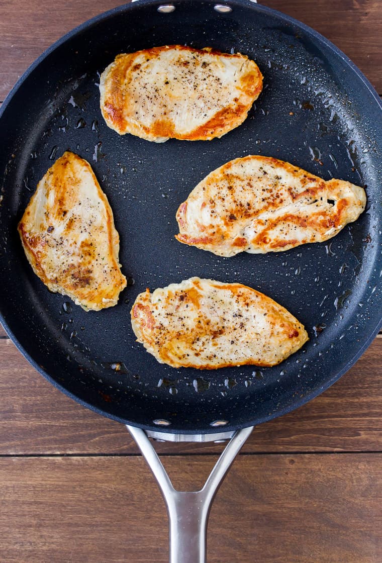 Overhead View of 4 Cooked Chicken Breasts in a Black Skillet on a Wood Background