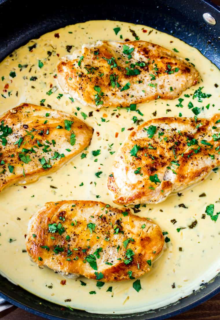 Close up of 4 chicken breasts in a cream sauce cooking in a black skillet