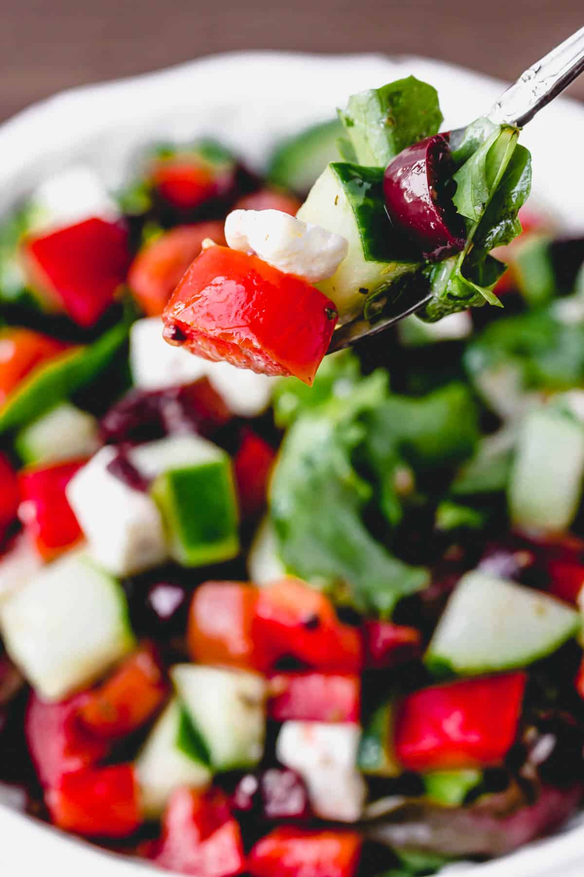 A fork full of Greek salad with the rest of the salad in the background