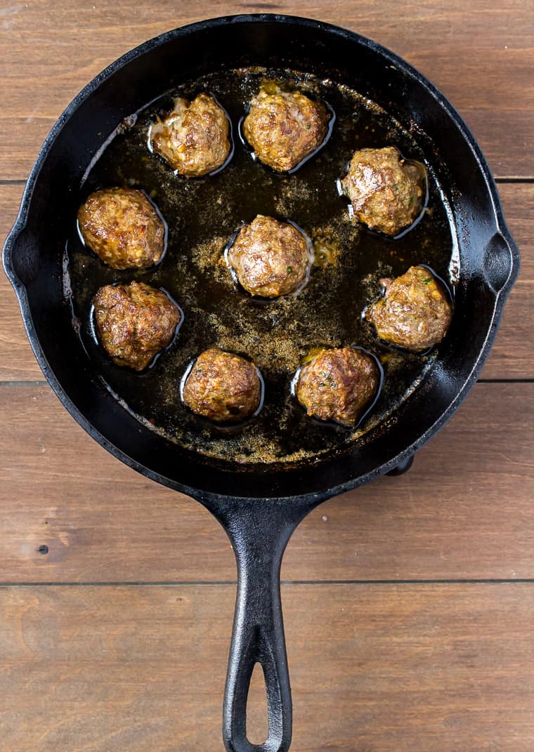 9 Meatballs Frying in a Cast Iron Skillet on a wood background