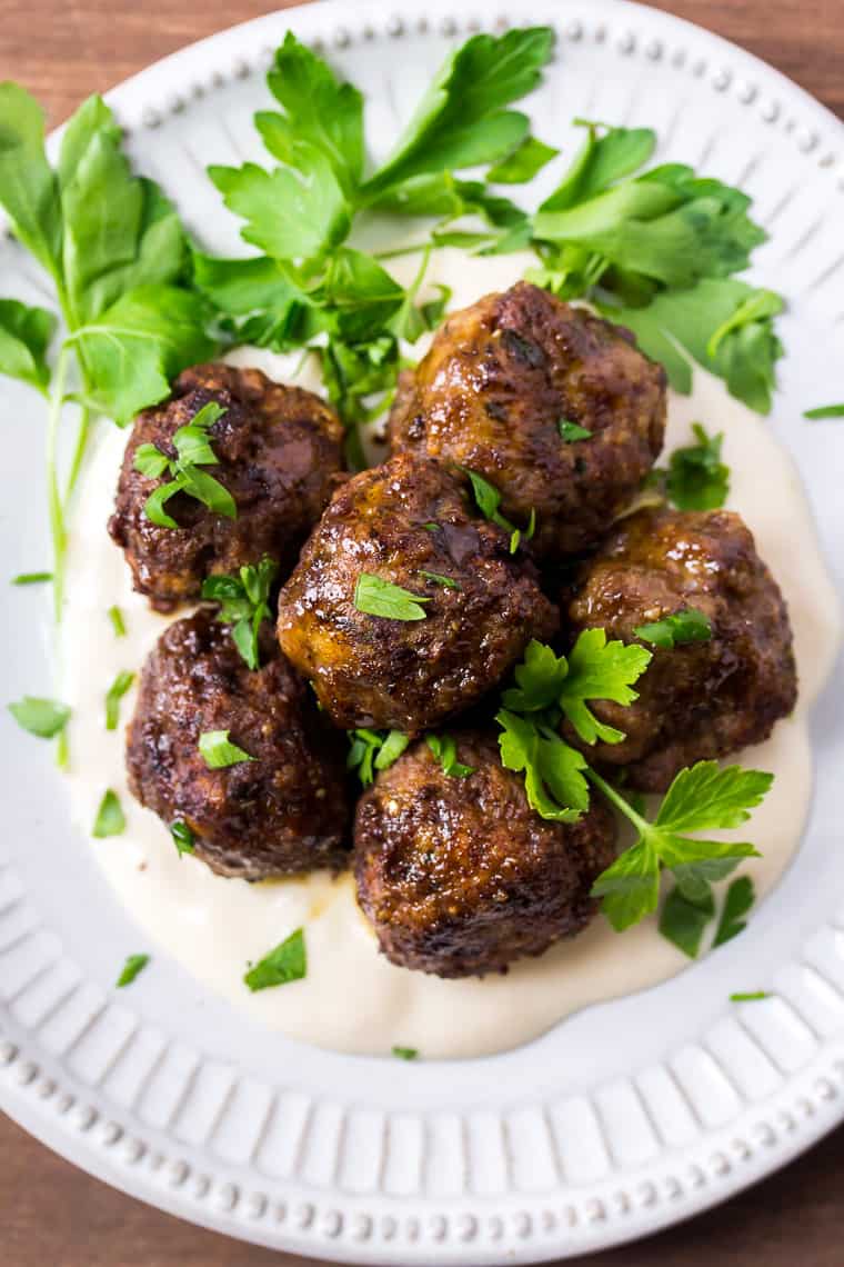 Close up of 5 Italian Meatballs on a White Plate with Parsley on a Wood Backdrop