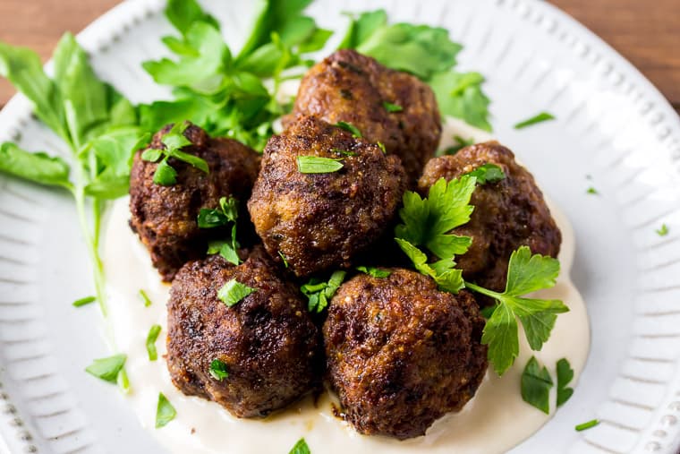 Close up of the Keto Italian Meatballs on a White Plate with Parsley and a wood background