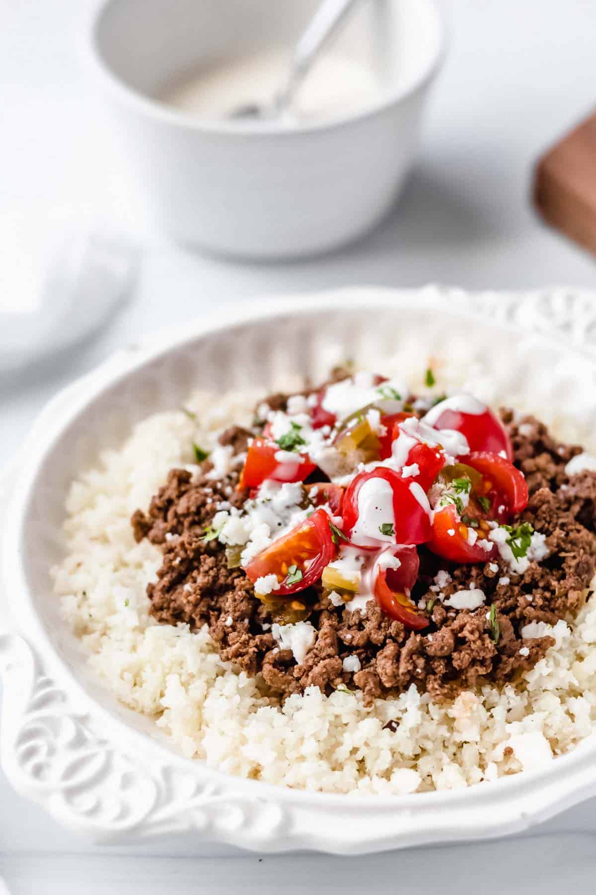 Close up of Keto Mexican Beef Bowls in a white bowl over a white background with a white bowl of sauce behind it
