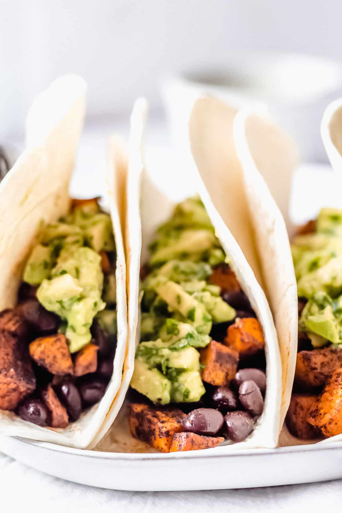 3 vegetarian sweet potato black bean tacos standing up on a white plate