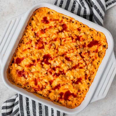 Overhead view of a buffalo chicken cauliflower casserole in a white, square casserole dish over a blue and white striped linen.