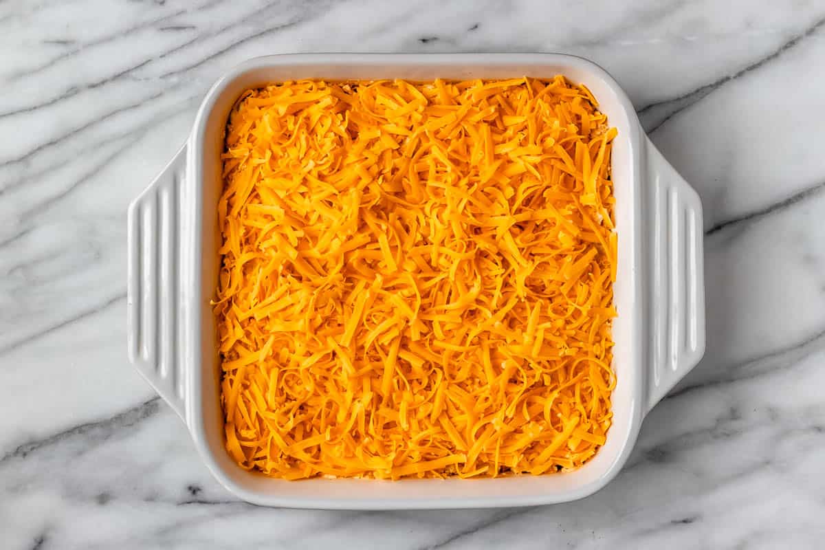 Buffalo chicken casserole topped with cheddar cheese in a white, square casserole dish.