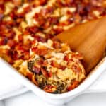 Cheesy Chicken and Broccoli casserole with bacon on top and a wood spoon lifting some up.