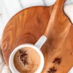 Overhead of a coconut chai latte in a white mug on a wood board with two star anise and spices on top with text overlay.