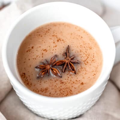 Close up of a coconut chai tea latte in a white mug with two star anise and spices on top.