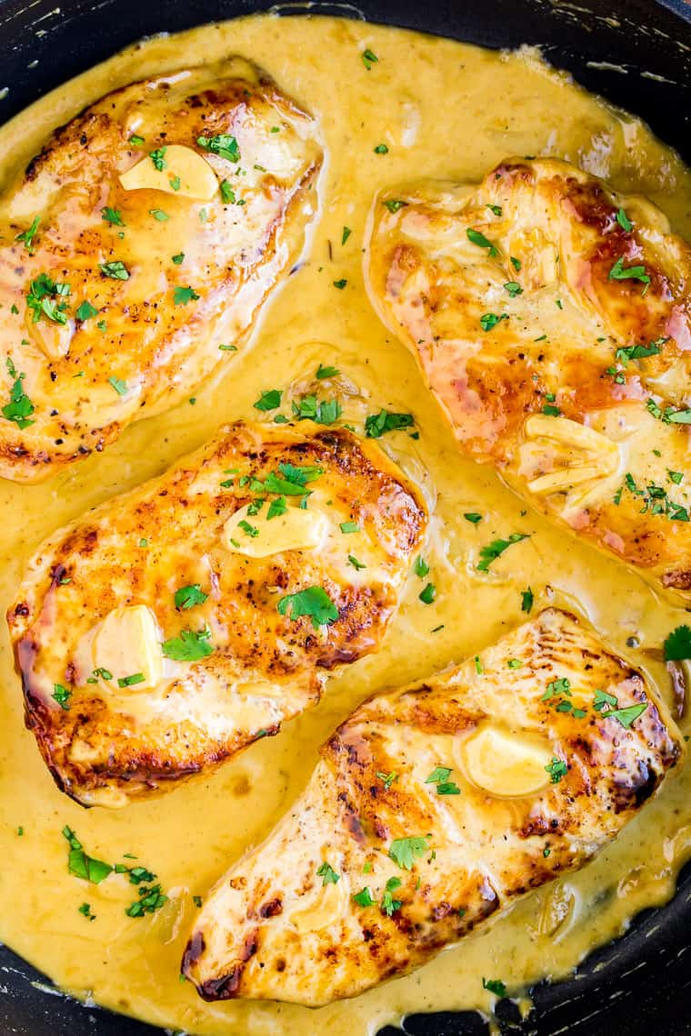 Close up of 4 Creamy Garlic Chicken Breasts in a Black Skillet Topped with Extra Sauce and Fresh Parsley 