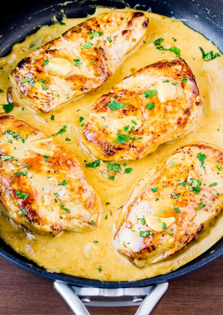 Close up of 4 Creamy Garlic Chicken Breasts in a Black Skillet Topped with Extra Sauce and Fresh Parsley all over a wood background