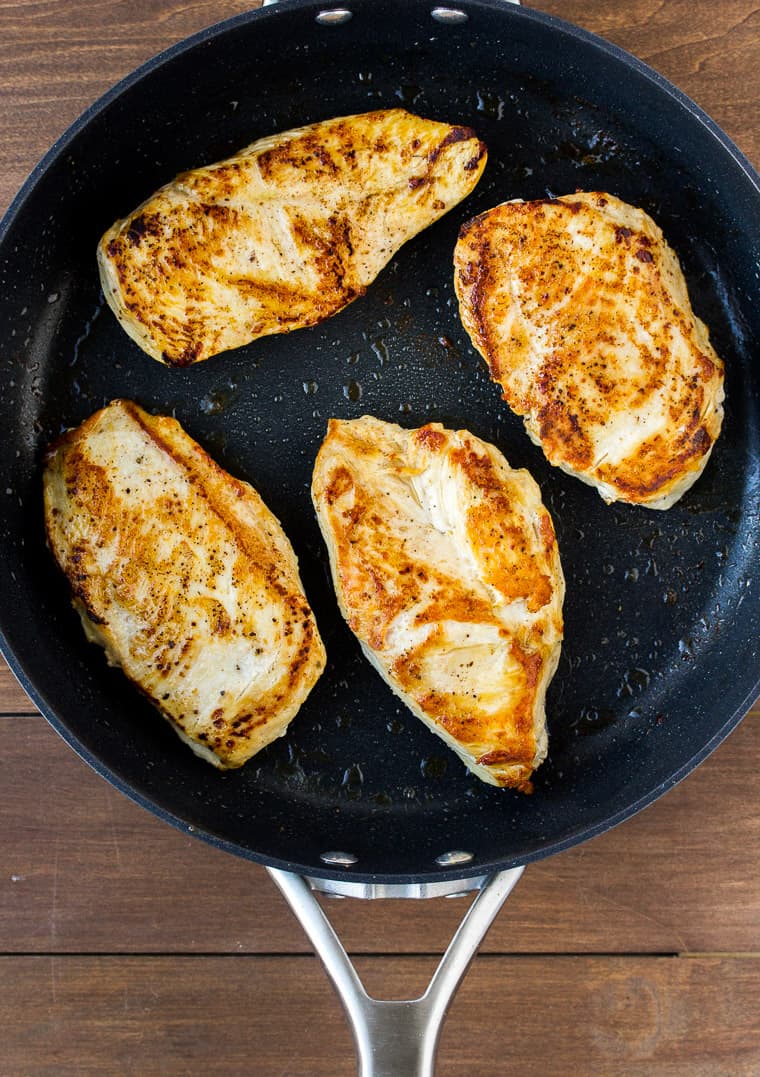 4 chicken breasts cooked in a black skillet on a wood background