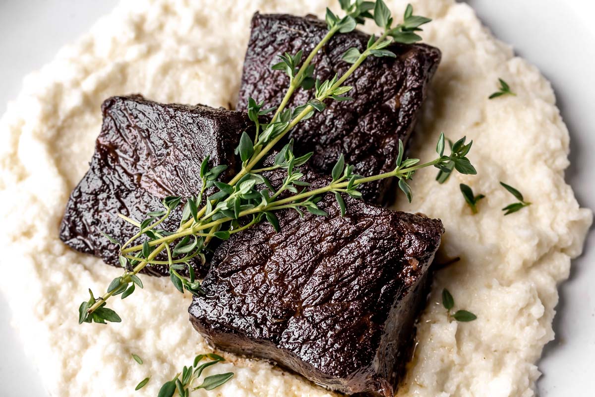 Close-up of short ribs of garlic butter on a bed of cauliflower puree with thyme garnish.